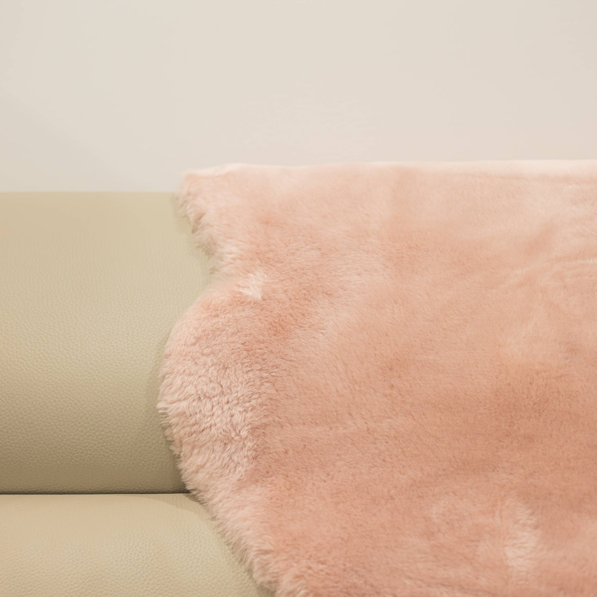 Blush sheepskin baby rug draped over seating showing dense wool texture and soft pink tone