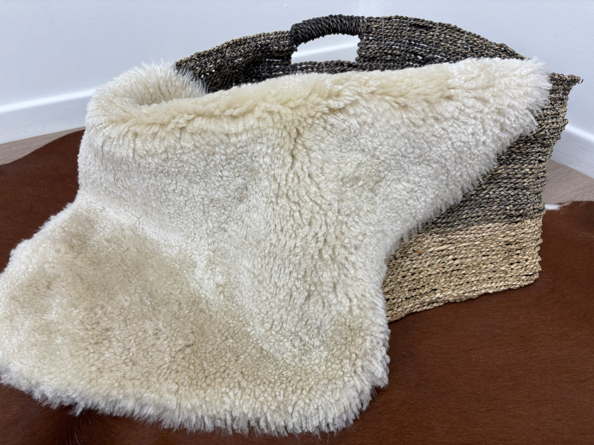Bone shearling rug draped over a woven basket showing short, tightly curled wool texture