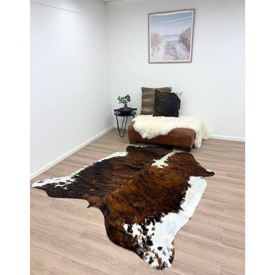 Tri colour cowhide rug styled in a neutral living space with ottoman and cushions