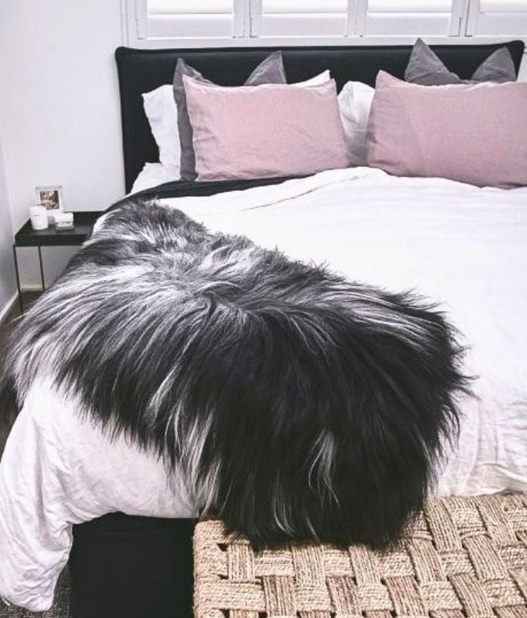 Icelandic sheepskin rug in a natural mix of tones styled over a bed in a bedroom setting