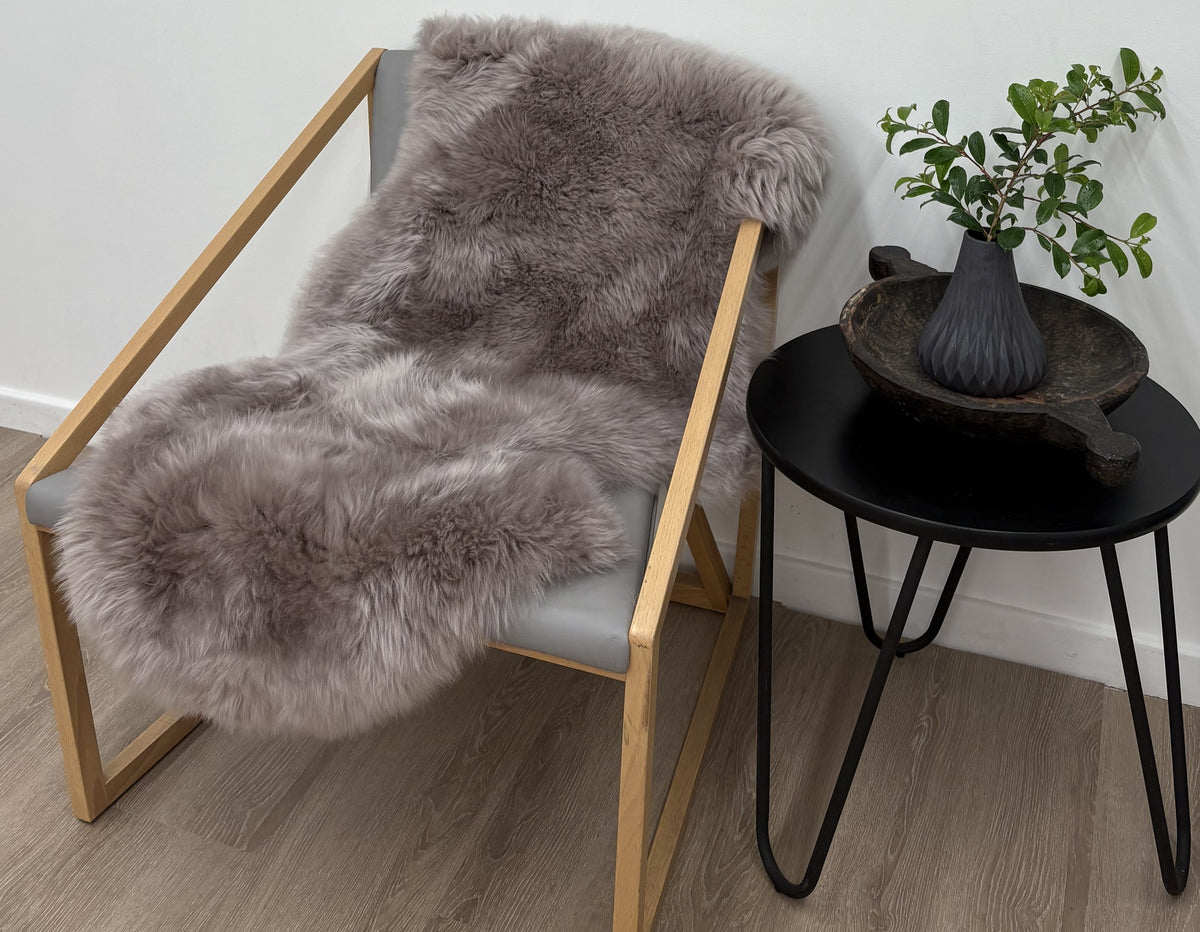 Merino sheepskin rug in mushroom tone draped over a chair styled in a neutral living space