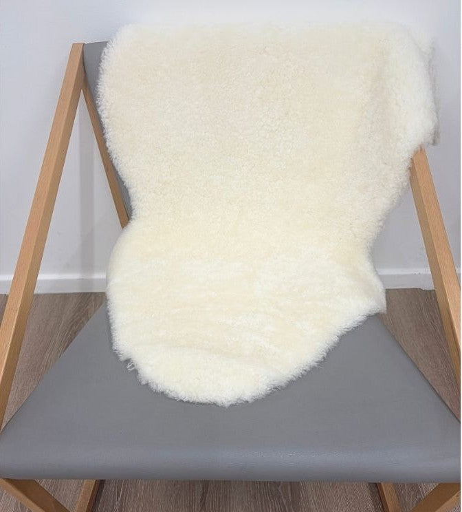 Natural white shearling sheepskin rug styled over a chair with dense wool and a soft, luxurious finish.