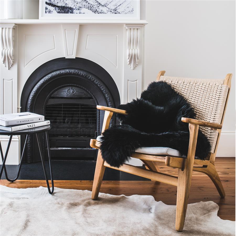 Black Merino sheepskin rug styled over armchair in living room