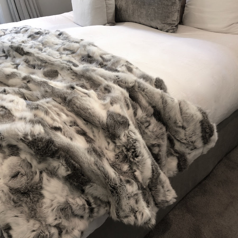 White and grey rabbit hide blanket draped over a bed showing natural hair texture and colour variation