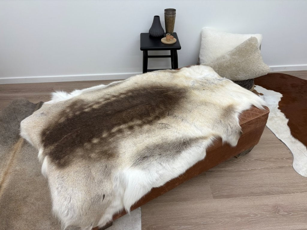 Beige reindeer hide throw draped over a bench showing natural markings and hair variation