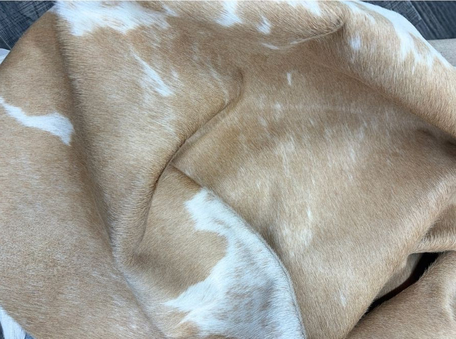 Premium beige and white cowhide rug close-up showcasing natural hair-on-hide texture, authentic markings and soft leather finish.
