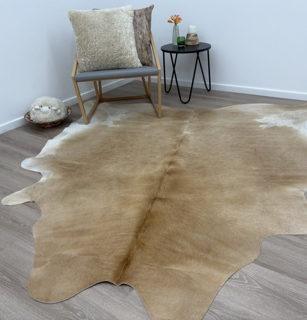 Beige and white cowhide rug styled in a living space on a timber floor
