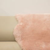 Blush sheepskin baby rug draped over seating showing dense wool texture and soft pink tone