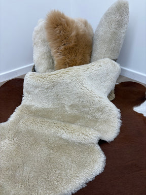 Bone shearling rug styled with other shearling hides showing short, tightly curled wool texture