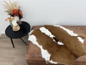 Natural brown and white calf hide rug styled over a sofa in a modern interior