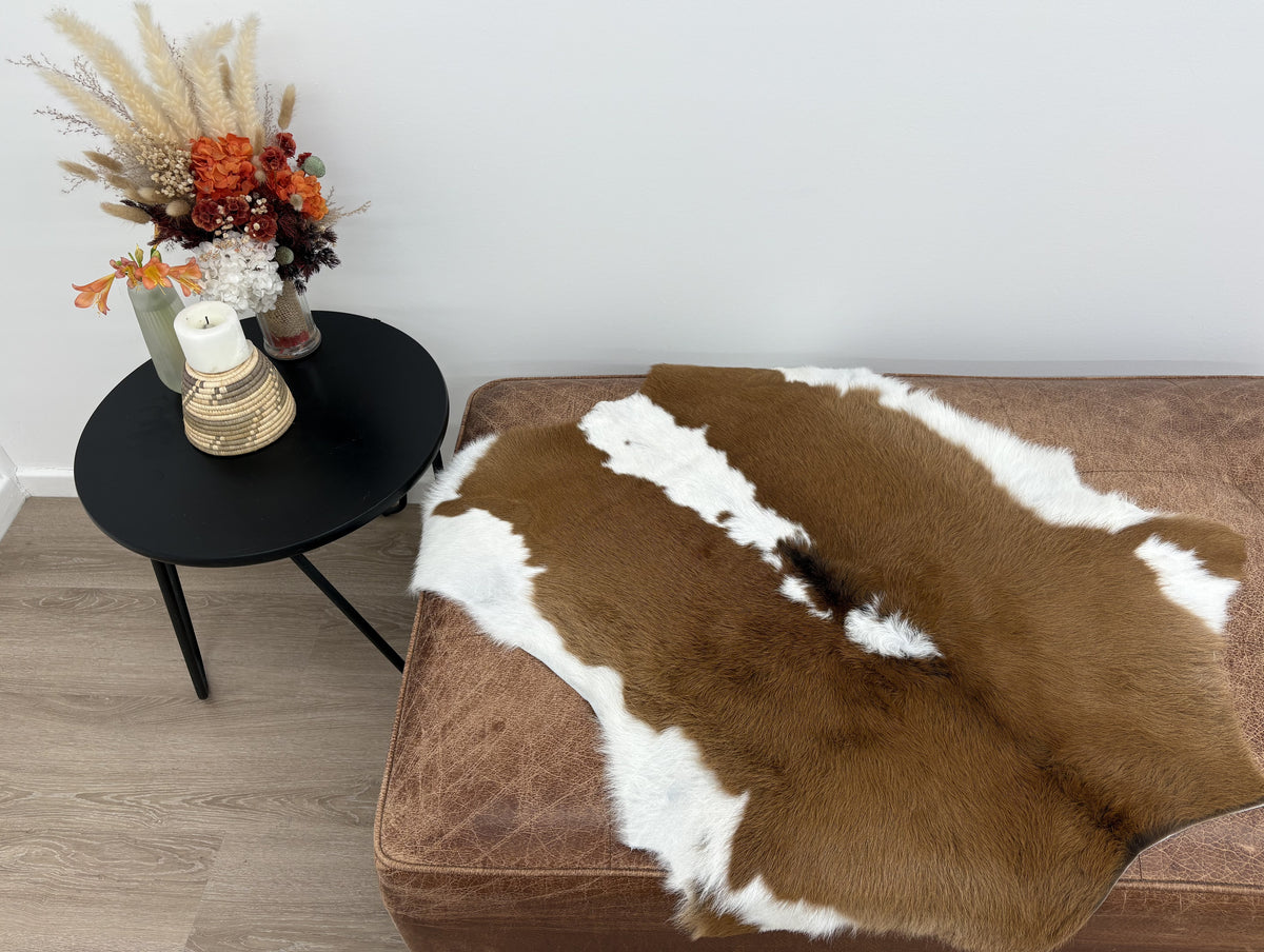 Brown and white calf hide rug styled over a leather ottoman beside a side table in a modern interior