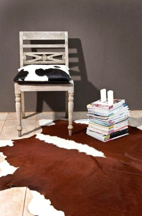 Brown and white Hereford cowhide rug regular size genuine hide with rich reddish tones styled in interior space with timber chair and stacked books