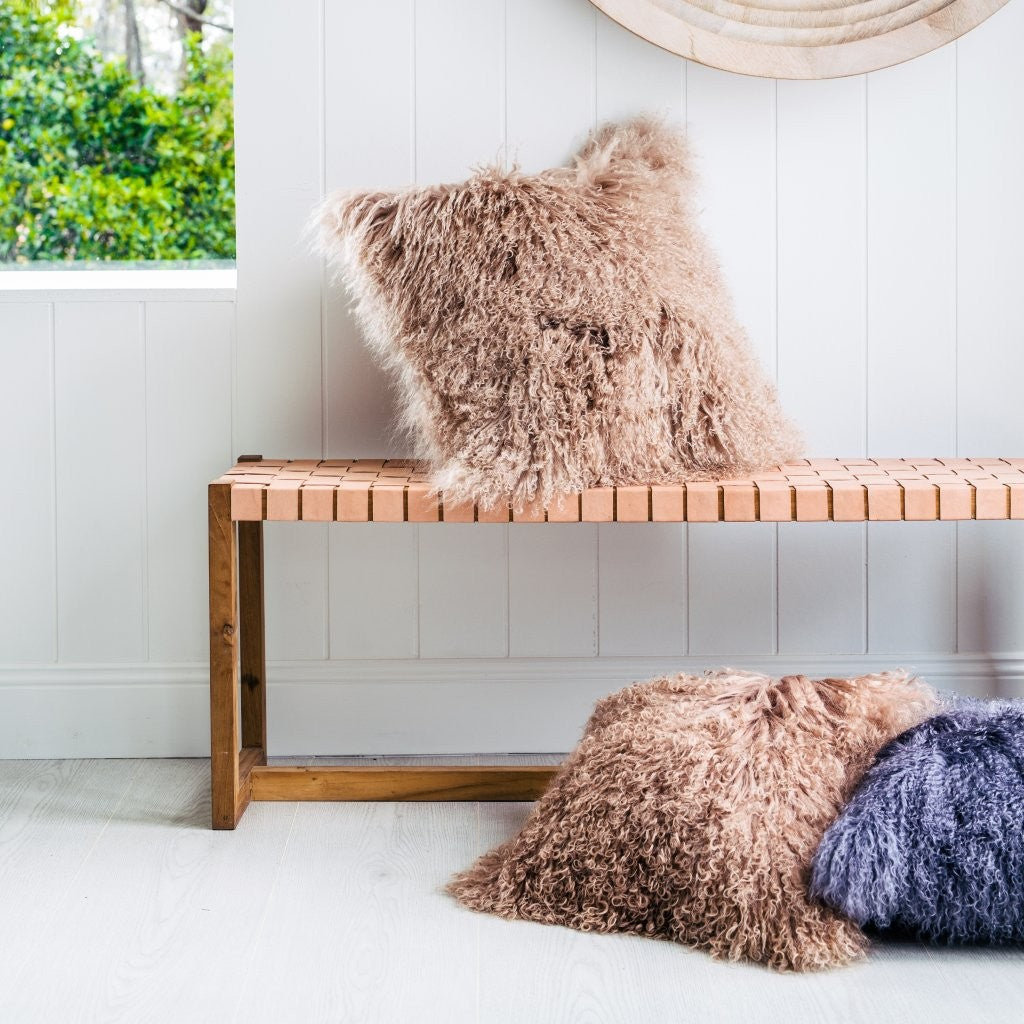Camel Mongolian sheepskin cushion with long curly fibres styled on a wooden bench with additional cushions in a bright interior