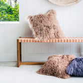 Camel Mongolian sheepskin cushion with long curly fibres styled on a wooden bench with additional cushions in a bright interior