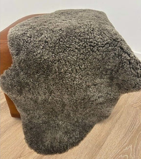 Chocolate fleck shearling sheepskin rug styled over a leather ottoman with dense, tightly curled wool and rich flecked colouring.
