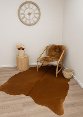 Small beige cowhide rug in warm honey tones styled beside a lounge chair