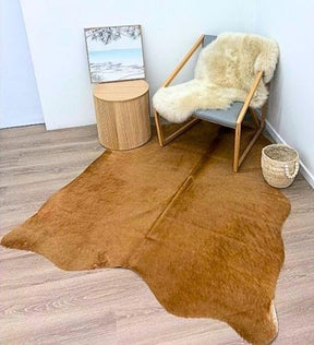 Beige small cowhide rug styled in a neutral interior with chair and side table
