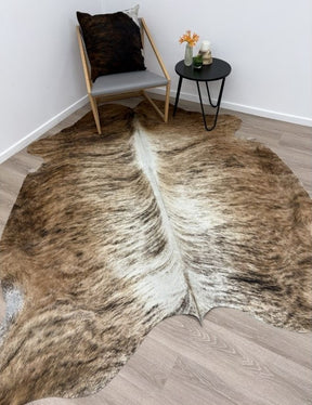 Large exotic brindle cowhide rug styled on a timber floor with a chair and small side table