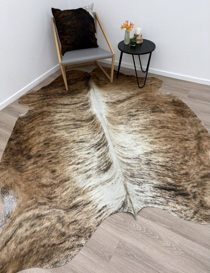 Large exotic brindle cowhide rug styled on a timber floor with a chair and small side table
