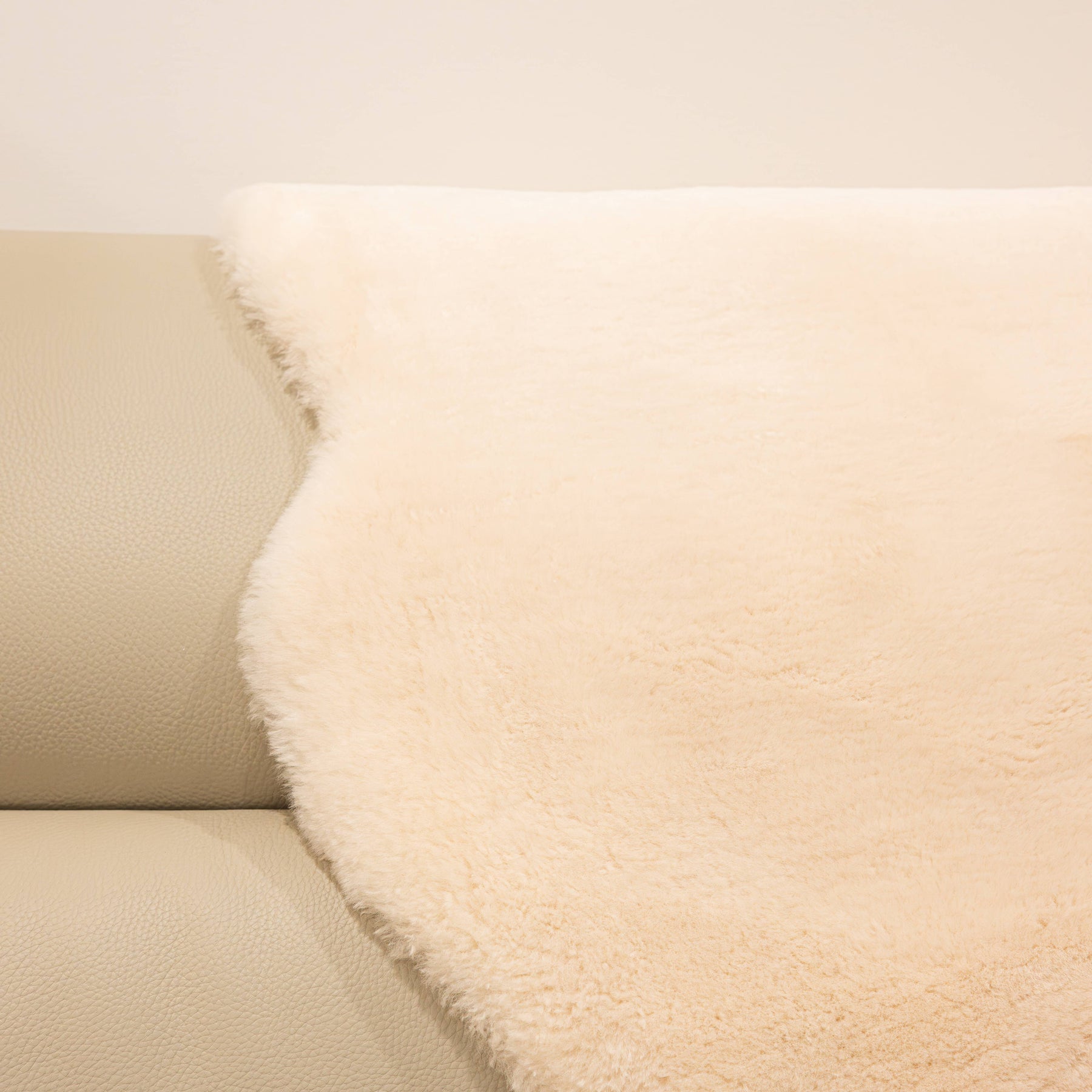 Dusk sheepskin baby rug draped over seating showing dense wool texture and warm neutral tone