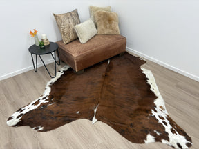 Exotic brindle cowhide rug styled in a lounge room with a sofa, cushions and side table on a timber floor