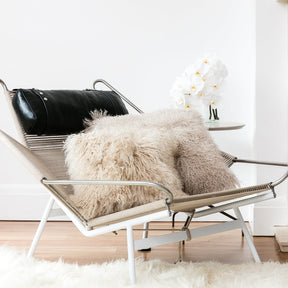 Fawn Mongolian sheepskin cushion with long hair texture styled on a modern chair in a light, neutral interior