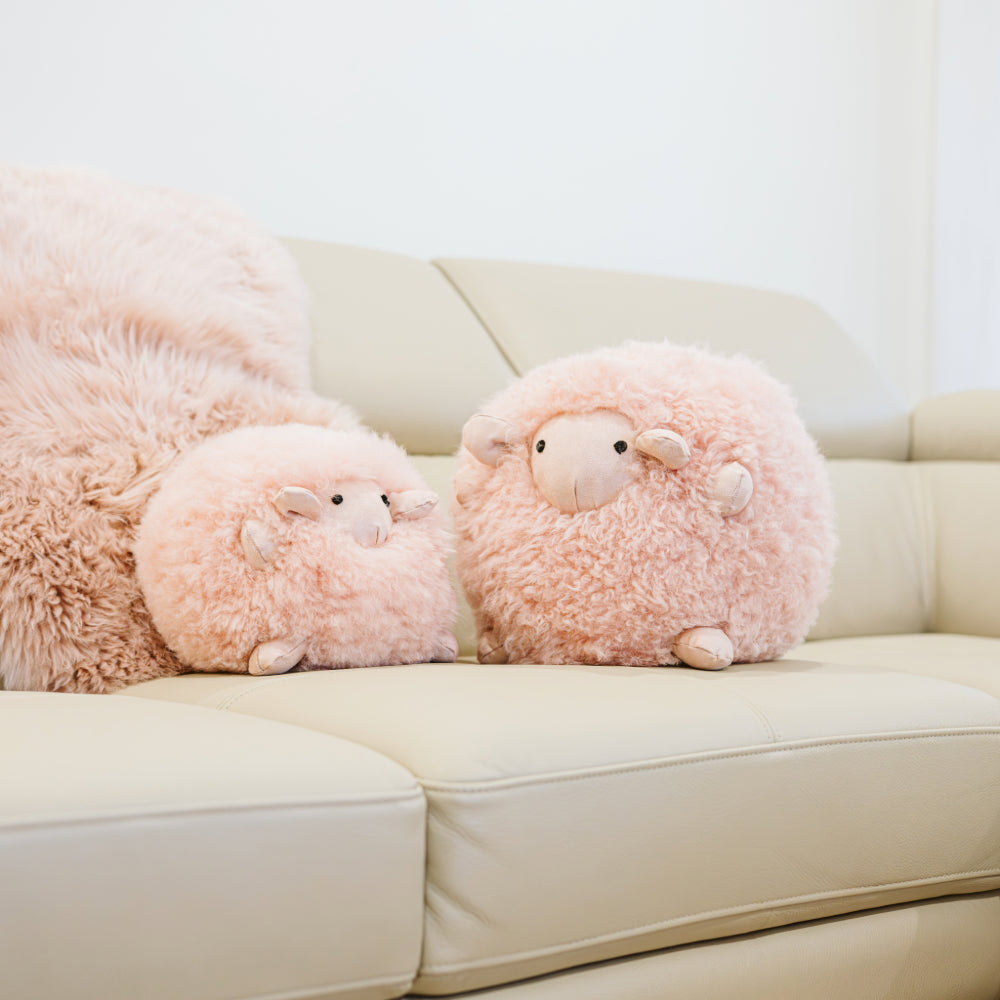 Two blush sheepskin toys made from natural sheepskin styled on a sofa