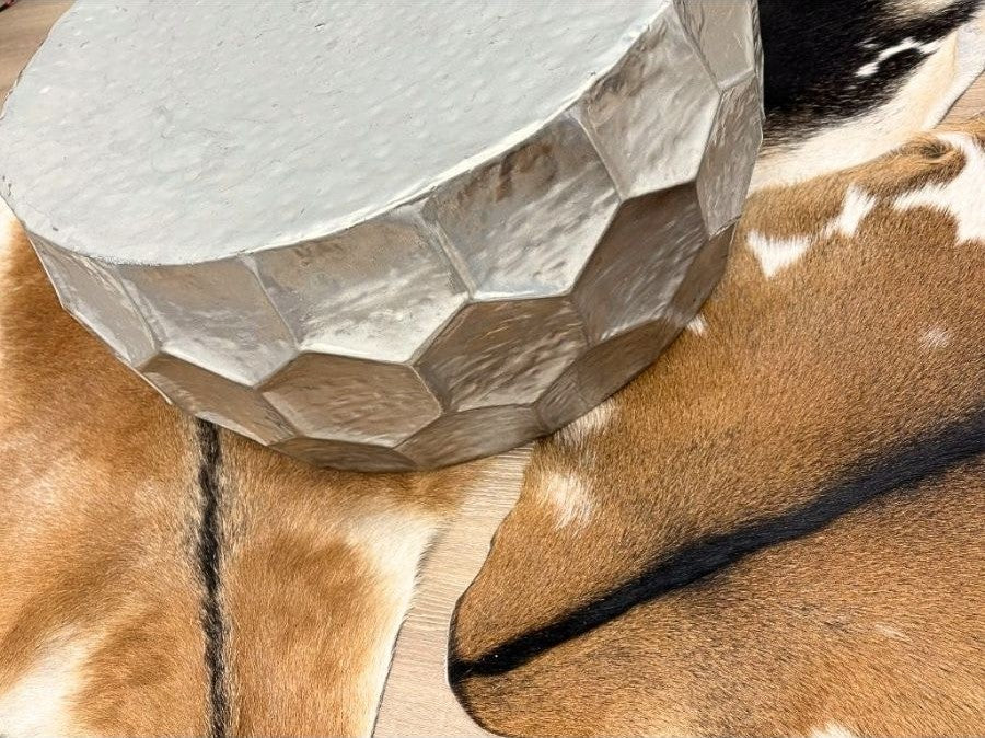 Natural goatskin hide rug styled beneath a metallic side table, showing texture and markings