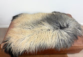 Greenlandic sheepskin rug displayed as a full hide with long crinkled wool in natural grey and ivory tones on a leather bench