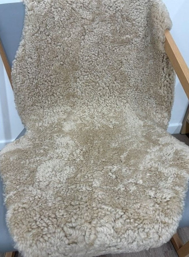 Honey shearling sheepskin rug styled over a chair, showcasing dense curled wool and a natural texture.