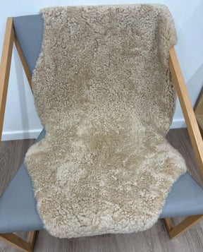 Honey shearling rug styled over a chair with dense curly wool and warm golden beige tones.