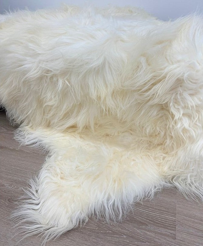 Close-up view of the edge of a natural white Icelandic sheepskin floor rug made from three hides stitched together, showing long wool texture