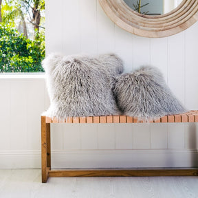 Light grey Mongolian sheepskin cushions styled on a timber bench in a bright interior with white walls and round mirror