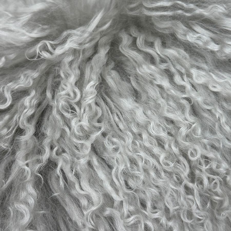 Close-up of light grey Mongolian sheepskin lumbar cushion showing long, naturally curly hair texture