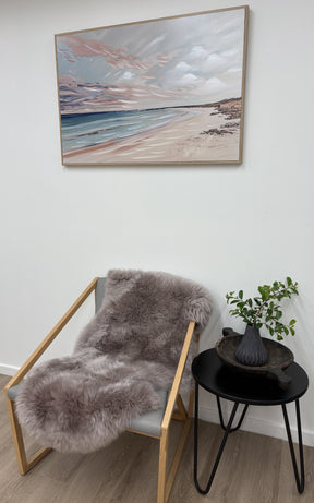 Merino sheepskin rug in mushroom tone draped over a chair in a neutral interior