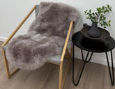 Merino sheepskin rug in mushroom tone draped over a chair styled in a neutral living space