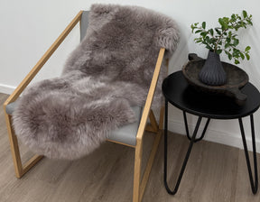 Merino sheepskin rug in mushroom tone draped over a chair styled in a neutral living space
