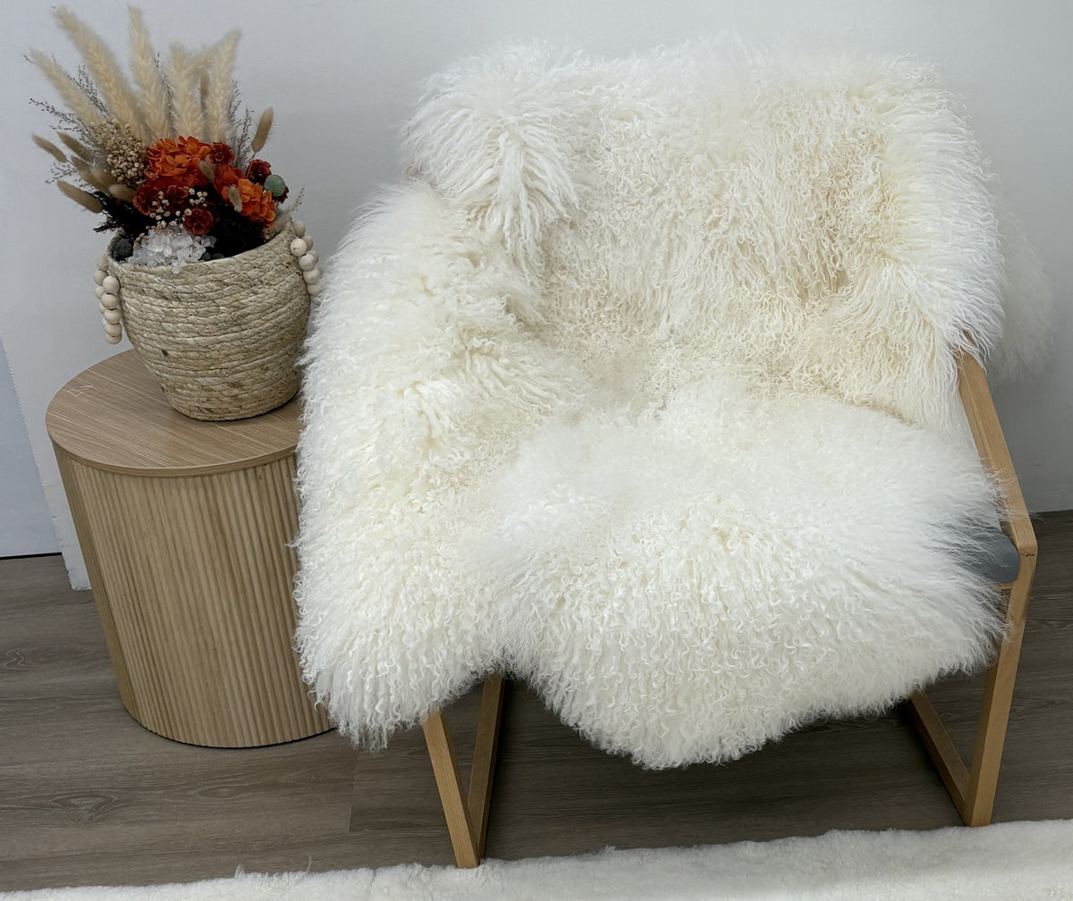 Natural white Mongolian sheepskin area rug made from four hides, styled over a wooden lounge chair