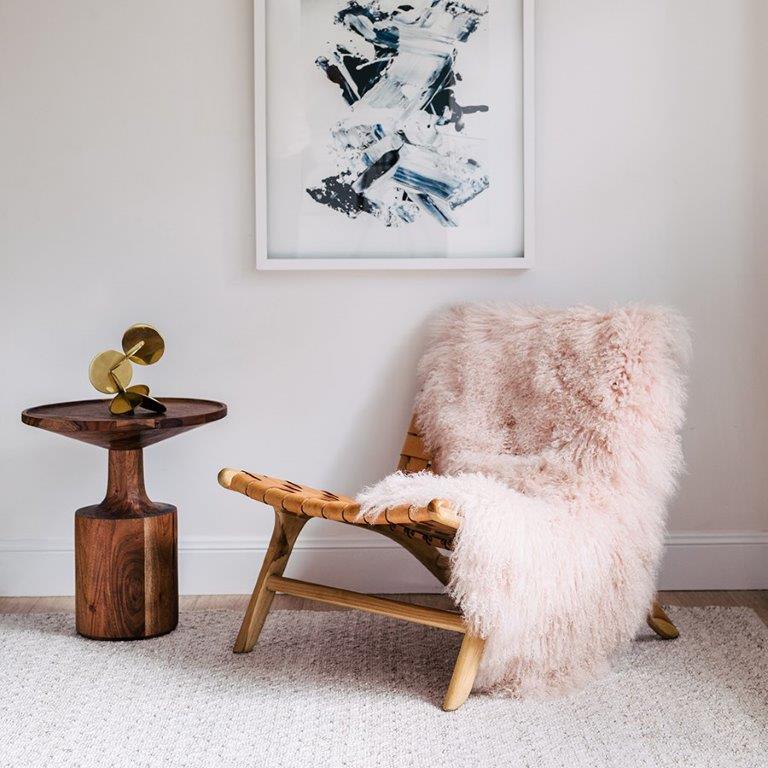 Blush Mongolian sheepskin rug styled over a wooden chair in a softly lit living space