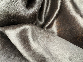 Close-up detail of a natural black cowhide rug showing smooth hair texture and subtle tonal variation