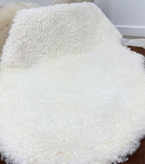 Natural white shearling rug draped over furniture showing short, tightly curled wool texture