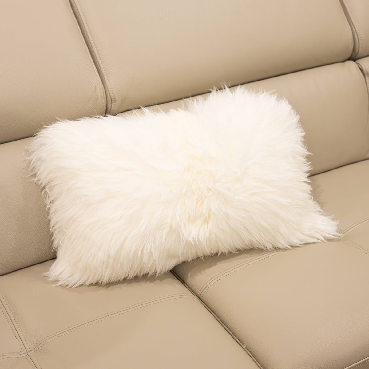 New Zealand sheepskin lumbar cushion in natural white with soft long wool texture displayed on a beige sofa