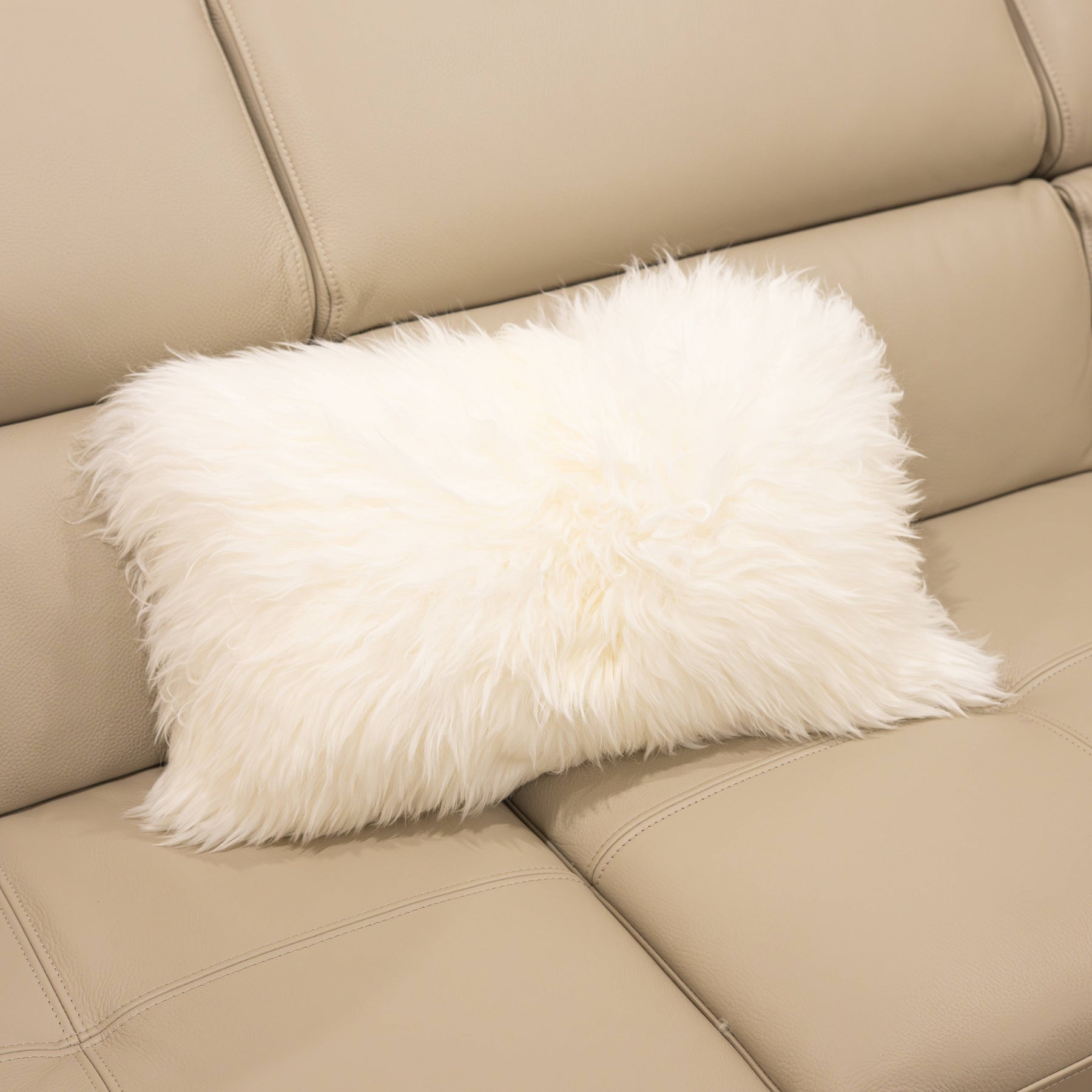 New Zealand sheepskin lumbar cushion in natural white with soft long wool texture displayed on a beige sofa