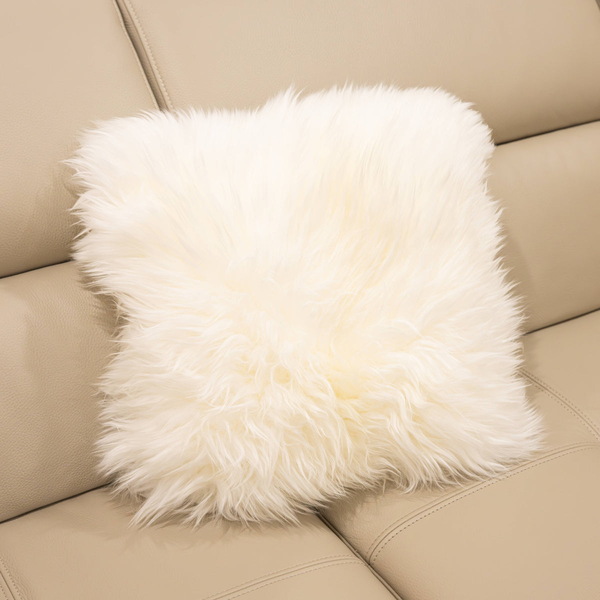 New Zealand sheepskin cushion in natural white with soft long wool texture displayed on a beige sofa
