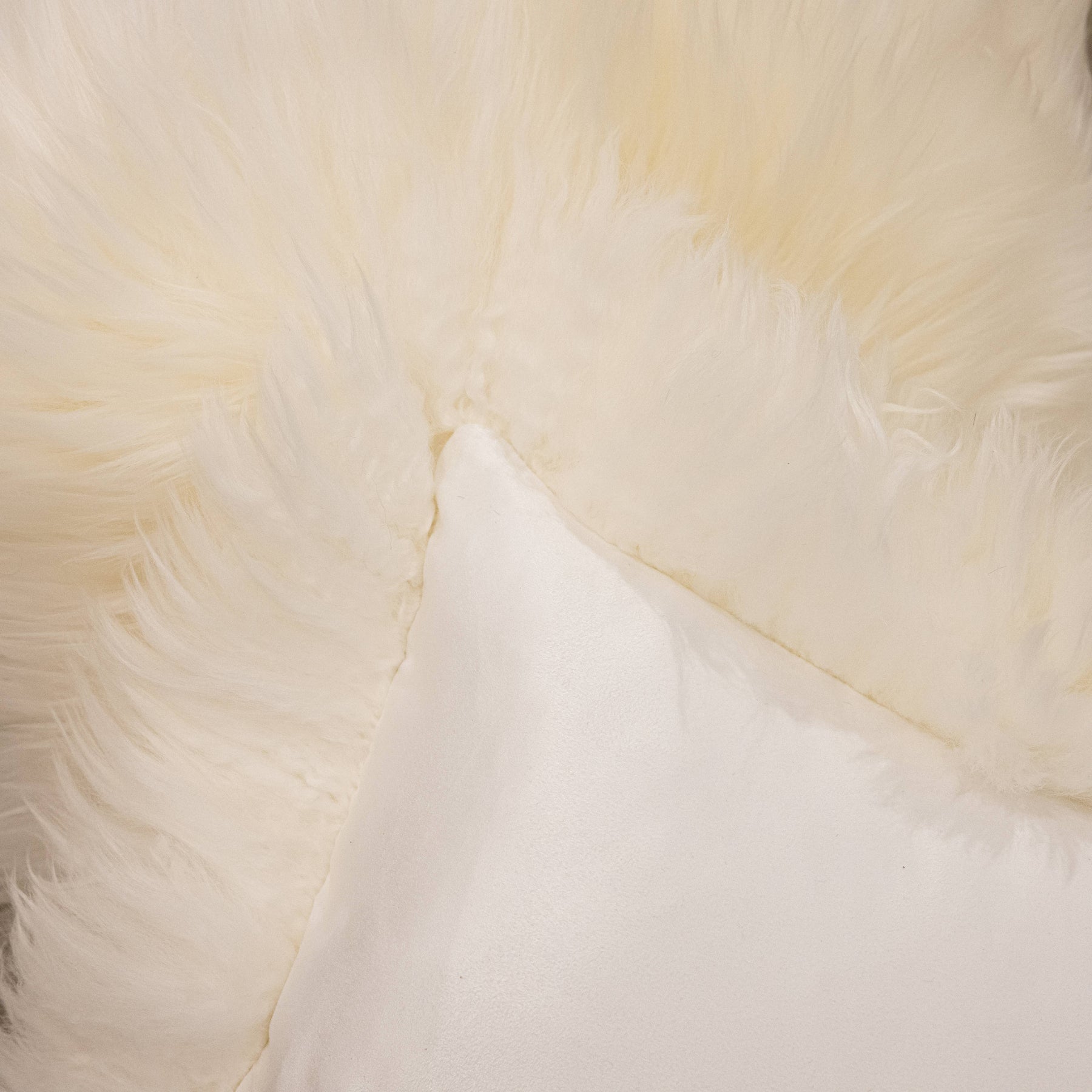 Close-up of New Zealand sheepskin cushion in natural white showing soft long wool front and fabric backing detail
