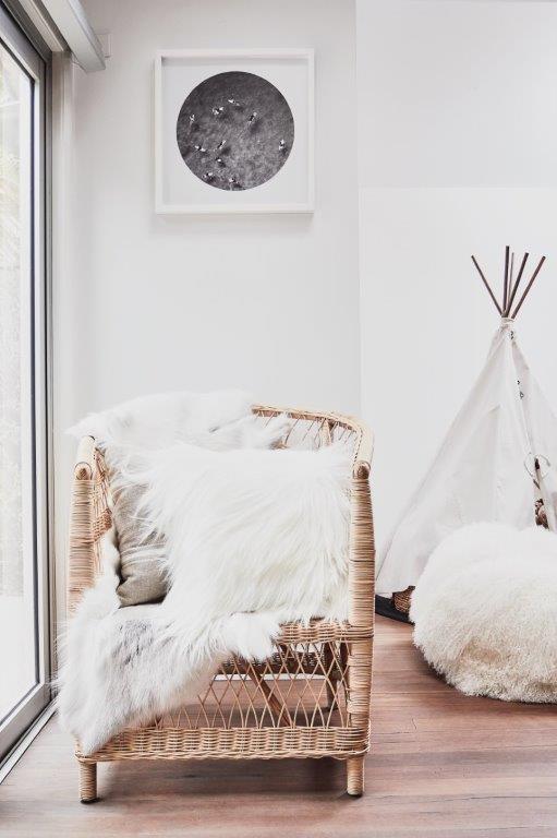 New Zealand sheepskin cushion in natural white styled on a wicker chair with soft furnishings in a bright interior setting