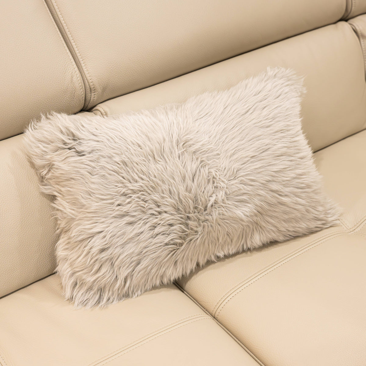 New Zealand sheepskin lumbar cushion in pale grey with plush long wool texture on a beige sofa