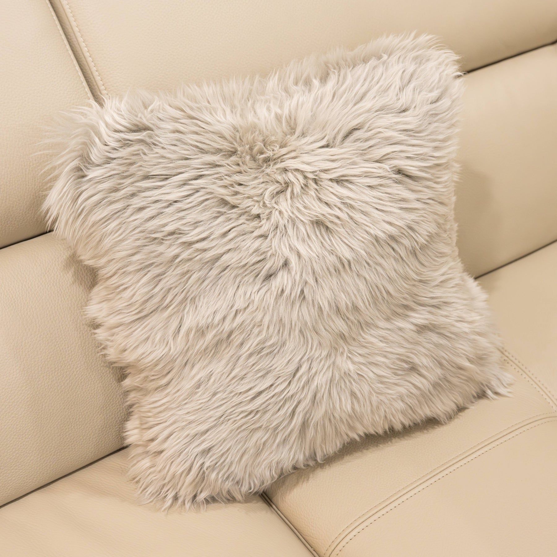 New Zealand sheepskin cushion in pale grey with plush long wool texture on a beige sofa