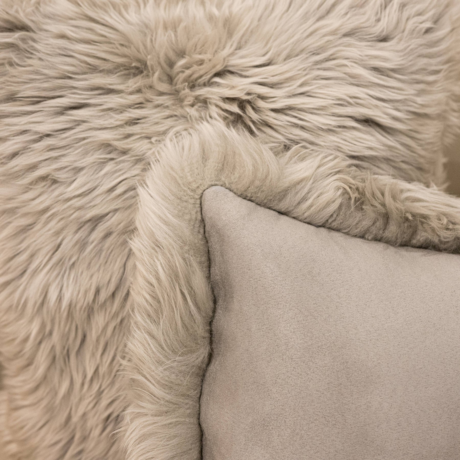 Close-up of New Zealand sheepskin cushion in pale grey showing soft long wool texture and backing detail