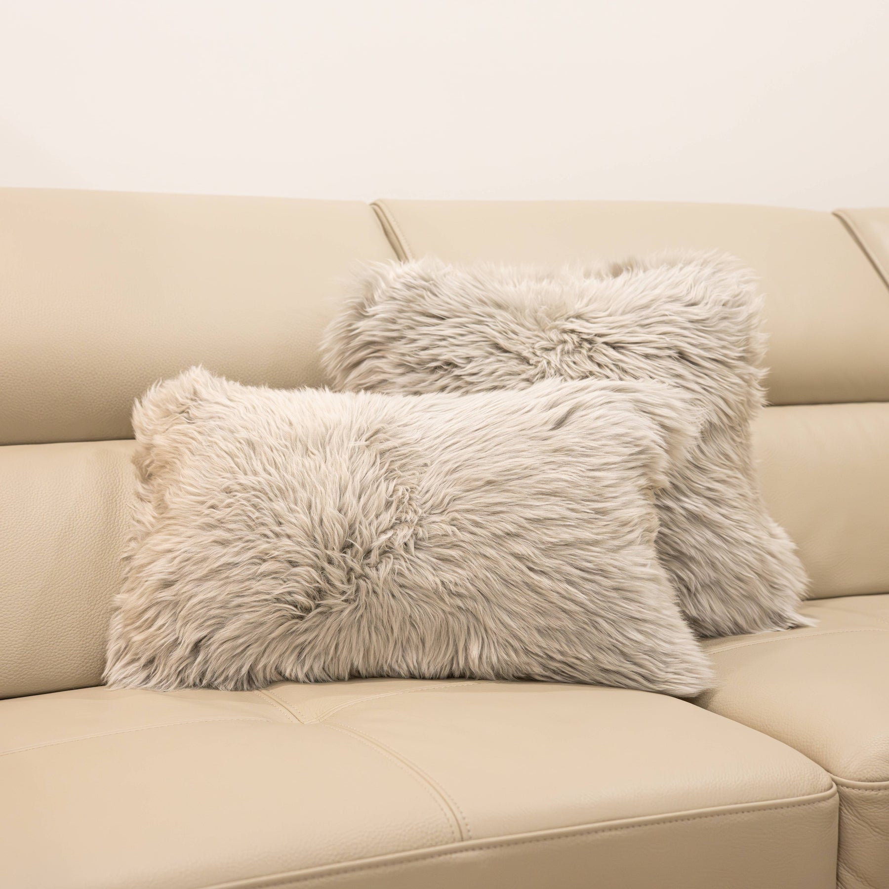 Two New Zealand sheepskin cushions in pale grey displayed on a beige sofa
